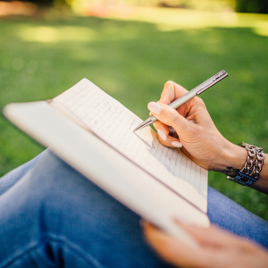 Primer plano de una persona sentada en el parque escribiendo un diario