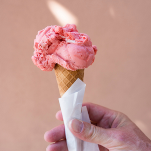 person holding an ice cream cone with strawberry ice cream