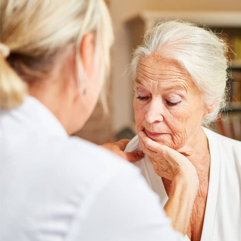 A healthcare provider examines an elderly woman's jaw/neck area during a medical consultation.