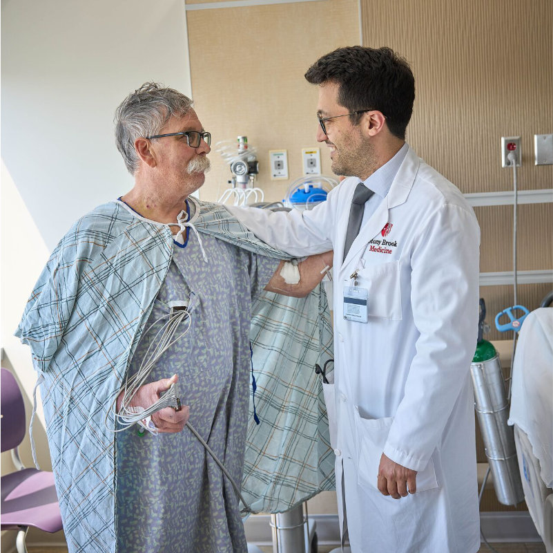 A doctor assisting an elderly male patient in a hospital gown.