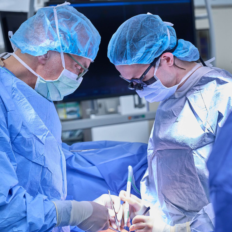 Two surgeons in scrubs and masks perform a surgical procedure in an operating room.