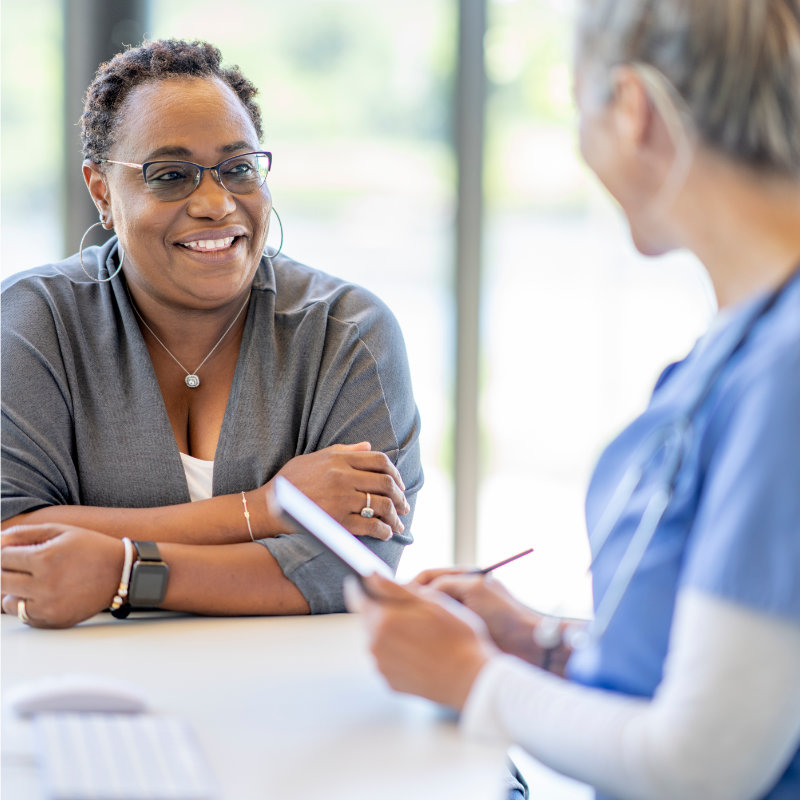 A female patient with glasses smiles during a consultation with a healthcare provider at a desk.