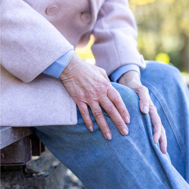 A close-up of an elderly person's hands resting on their knee, suggesting joint discomfort.