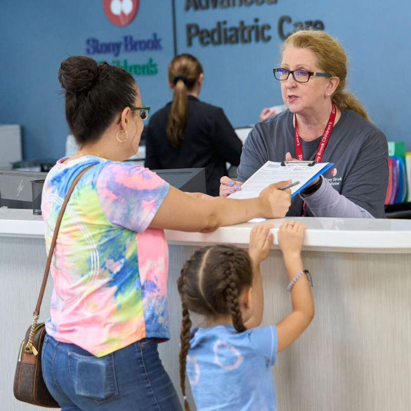 Mother and child checking in at a pediatric care reception desk.