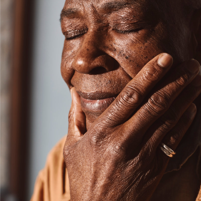 Close-up of an elderly woman holding her cheek, in discomfort.
