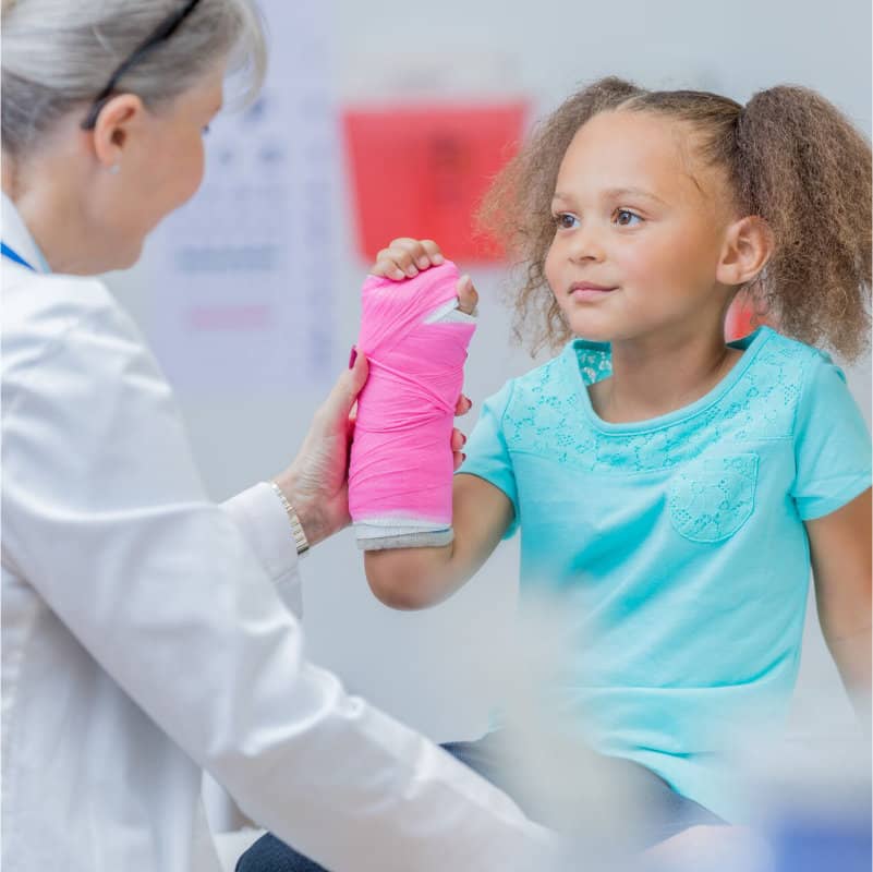 A young girl with a pink cast on her arm smiles at a female doctor in a clinic.