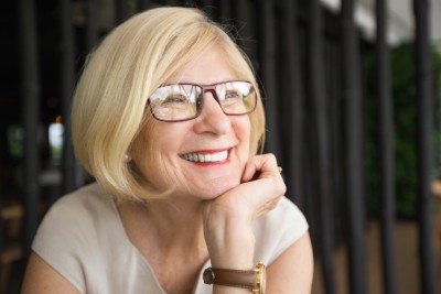 blonde woman with glasses smiling with her hand under her chin
