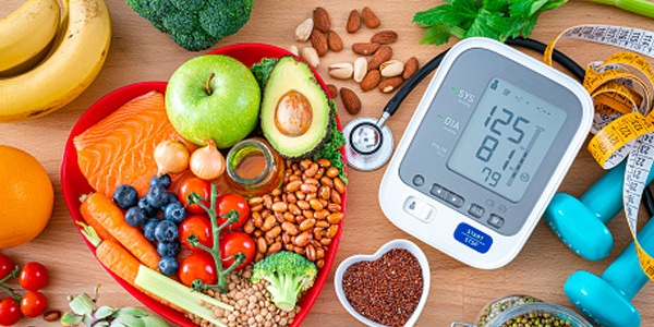 Overhead view of a group of food that contains healthy nutrients for heart care, a blood pressure monitor, dummbells, tape measure and sthetoscope shot on wooden table.