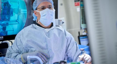 A healthcare professional in surgical gear monitors a medical imaging screen in a clinical setting.